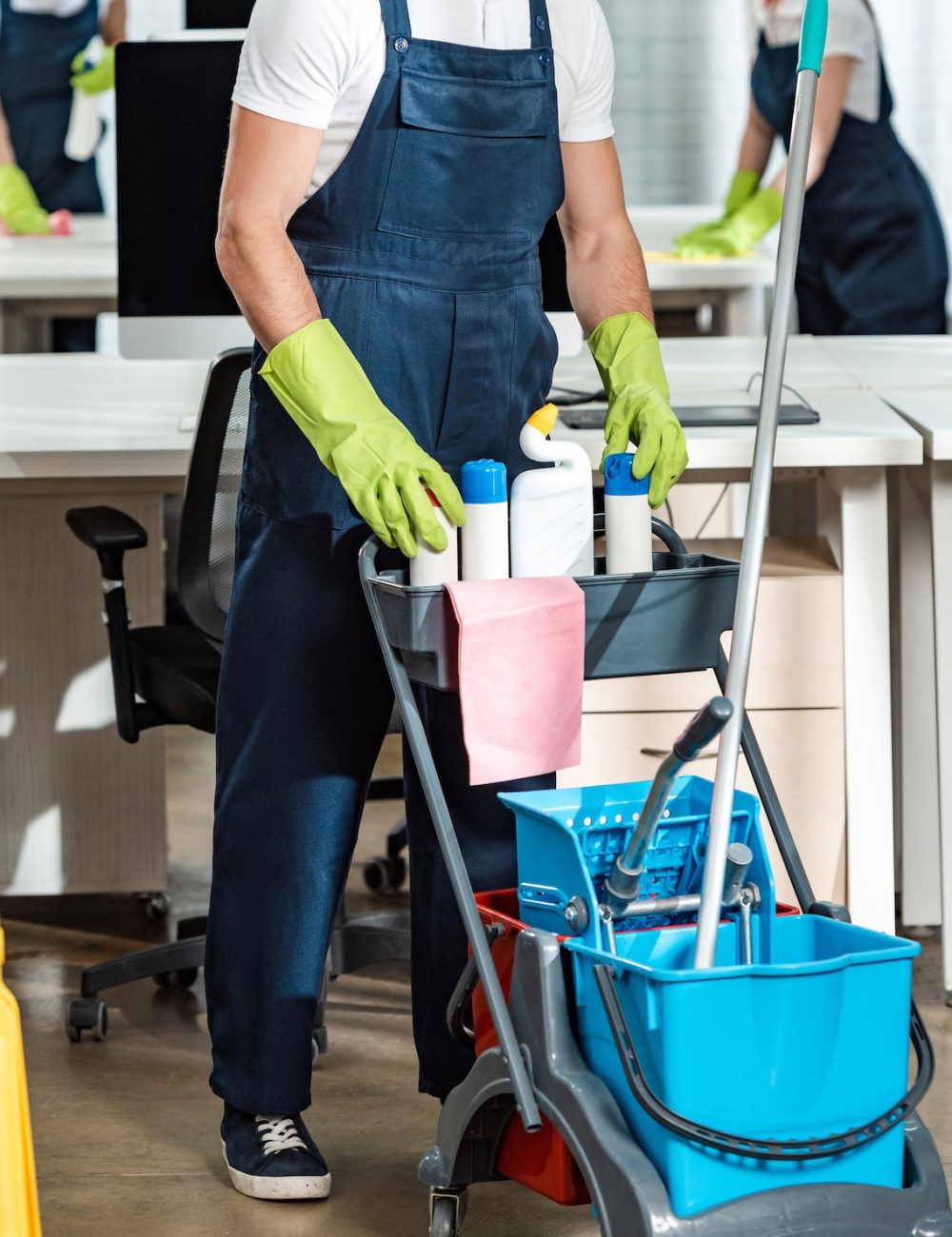 young-cleaner-standing-near-cart-with-cleaning-supplies